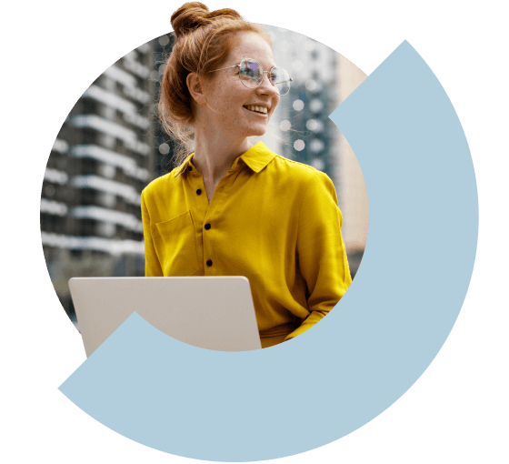 Eine Frau lächelt, während sie draußen am Laptop arbeitet.