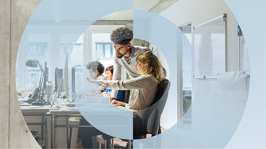 Zwei Mitarbeitende in einem Büro betrachten den Bericht „The Pulse of Work in 2025“ auf einem Computer.